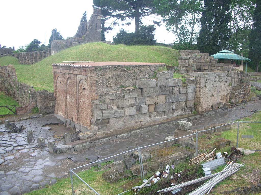 Vesuvian Gate, Pompeii. May 2010. 
Looking north-west from south end, with Castellum Aquae leaning against west wall, in centre, with narrow sidewalk, and Tower X, in background. 
On the left are lava cippi, as described by Sogliano, and apparently acting as kerbstones. Photo courtesy of Ivo van der Graaff.
According to Van der Graaff –
“The Porta Vesuvio witnessed extensive changes when it became the designated site for the arrival of an aqueduct…….
The water castellum (distribution tank) on the west flank of the gate is the terminus of a branch of the Serino aqueduct built by Augustus to supply the Roman naval base at Misenum around 35 BCE (See Fig. 3.4 and Note 73). ……………….
A new wide plaza in front of it further stressed the presence of the castellum to onlookers. ………………
The setting created around the castellum was largely symbolic. 
The fortifications – the agger, gate, and nearby Tower X in particular – framed the building and further stressed the status of both structures as civic monuments.
The aqueduct and its terminus was a new civic monument that affected the fortifications that had constituted a symbol of Samnite Pompeii. This hallmark of Samnite Pompeii was now obfuscated in one of the most visible and militarily powerful areas of the fortifications. The Porta Vesuvio would become a landmark of the Augustan urban renewal. It would maintain this role through the rest of Pompeian history.”
See Van der Graaff, I. (2018). The Fortifications of Pompeii and Ancient Italy. Routledge, (p.127-128).

