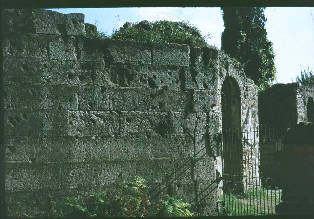 Pompeii Porta Ercolano or Herculaneum Gate east side. Looking south towards city walls.
Photographed 1970-79 by Günther Einhorn, picture courtesy of his son Ralf Einhorn.
See Notizie degli Scavi, 1943, (p.275-294), 
for article entitled “Isolation of the wall between the Vesuvian Gate and Herculaneum Gate.”
(Isolamento della cinta murale fra Porta Vesuvio e Porta Ercolano).

According to Van der Graaff –
“Littered with scars from the Sullan siege, the fourteen-course section still displays some of the highest-quality finished masonry of the entire circuit (Note 75). It is also unique as the only stretch of fortifications composed entirely of tuff – a circumstance reflecting its prominent position next to the gate……….
The resulting effect set the stage for approaching viewers of the architectural character of the city behind the gate.”
See Van der Graaff, I. (2018). The Fortifications of Pompeii and Ancient Italy. Routledge, (p.65 and Note 75).
