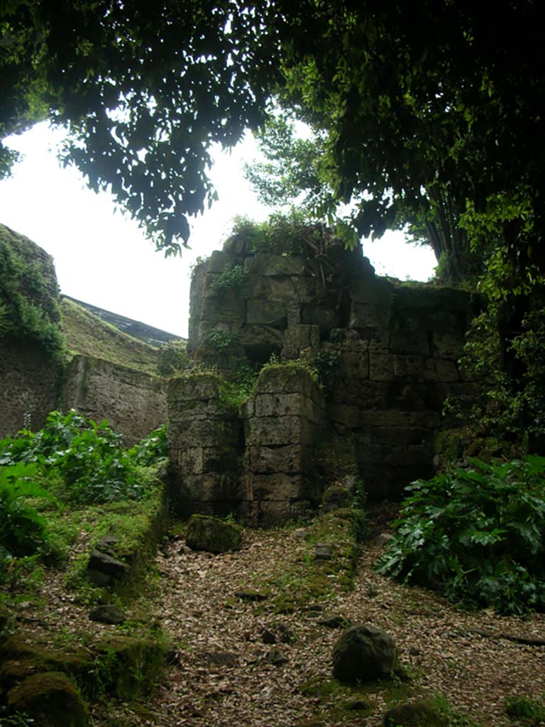 Walls on east side of Pompeii in north-east corner near Nola Gate. May 2010. 
Photo courtesy of Ivo van der Graaff.
According to Van der Graaff –
“The drain passing through the agger at the Porta Nola highlights how the formalization of water channels through the gates achieved an almost monumental status (see plate 18).
The inlet is an inconspicuous opening to the left of the steps leading up to the wall-walk. 
It collected rainwater from most of the Via di Nola, which, given its length, must have yielded a considerable amount. 
The channel through the agger is composed of concrete, implying that it is roughly contemporary with the gate’s vault dating to the second century BCE.
The opening on the opposite end is rather grand, sitting on a high base of travertine masonry extending out from the curtain wall.
The resulting petite bastion guided rainwater in a small cascade onto the road below, emphasizing the drainage of the Via di Nola every time substantial rain hit the city. Water has cut deep into the masonry, indicating that it functioned for a considerable period.
The masonry of the drain extension clearly abuts the curtain wall, indicating its later construction.
A striking feature is that engineers built the drain extension in travertine masonry in an effort to match the lower courses of the older adjacent wall curtain.”
See Van der Graaff, I. (2018). The Fortifications of Pompeii and Ancient Italy. Routledge, (p.104-5).
