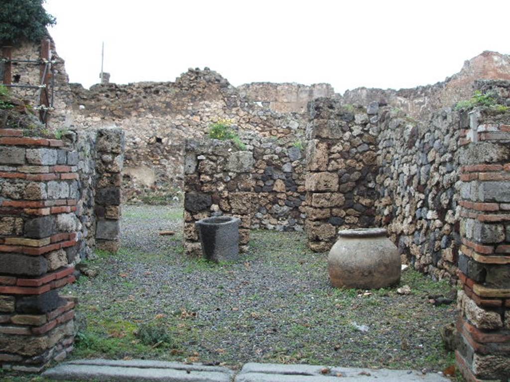 VII.16.4 Pompeii. December 2004. Looking north across shop towards doorway to atrium of VII.16.3, and doorway to rear room.
On the left, in the west wall was another doorway to the entrance corridor of VII.16.3.
According to Boyce –
in the east wall was a semi-circular niche (h.0.40, w.0.45, d.0.20, h. above floor 0.90) – la nicchia dei Penati, according to Fiorelli.
See Boyce G. K., 1937. Corpus of the Lararia of Pompeii. Rome: MAAR 14. (p.73, no.336) 
According to Garcia y Garcia, this workshop was destroyed by the bombing of 13th September 1943, and then partially restored in 1950.
There is now no trace of a window at the rear looking into the atrium, as it has been replaced by a doorway.
The niche that Boyce described as being in the east wall, although there was doubt as to its exact position, has not been replaced at all.
Avellino located it in the west wall, whereas Boyce said in the east wall.
See Garcia y Garcia, L., 2006. Danni di guerra a Pompei. Rome: L’Erma di Bretschneider. (p.131)

