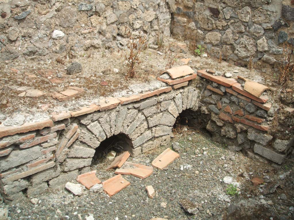 IX.5.14 Pompeii. May 2005.  Room “q”, kitchen.
Looking north-east towards hearth in kitchen (room “q”), on south side of peristyle, in servants’ area.
According to Boyce, on the south wall of this kitchen, was a fragmentary lararium painting.
Boyce said that Mau thought this kitchen was reserved for the use of the members of the household.
See Boyce G. K., 1937. Corpus of the Lararia of Pompeii. Rome: MAAR 14. (p.86, no.426).  
See Sogliano, A., 1879. Le pitture murali campane scoverte negli anni 1867-79. Napoli: (p.19, no.69)

