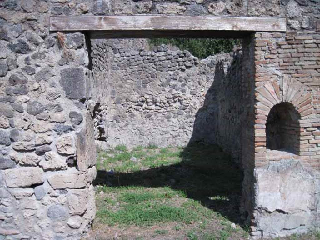 I.1.2 Pompeii. September 2010. 
Doorway to rear room in north-east corner, perhaps for the use of customers. 
Looking east. Photo courtesy of Drew Baker.

According to Warscher, quoting Mau in Bull. Inst 1875, p.26, 
“Dietro alla bottega a destra vi è la spaziosa cucina con focolare e cesso, a sinistra una stanza larga 2,96, profonda 5,24, dipinta negligentemente nello stile degli ultimi tempi di Pompei: i colori predominanti sono rosso nello zoccolo, giallo nella parte media, bianco in quella superiore.  
Sul muro di S troviamo un quadro alto 0,30, largo 0,40, rappresentante la morte di Elle.  Il fondo è tutto riempito di color turchino che rappresenta il mare. Sull’ariete che corre verso destra, sta seduto Frisso, rivolto allo spettatore e la coscia destra, come pare, coperta d’una veste bianca, tenendosi colla sinistra al collo dell’ariete, mentre stende la destra ad Elle, che dietro l’ariete affonda nel mare, alzando verso il fratello ambedue le mani.
Sul muro di E un altro quadro molto mal conservato, alto 0,38, ed altrettanto largo, ci mostra Apolline ritto in piede e rivolto a sinistra, verso la qual parte stende la man destra, mentre sopra la spalla sinistra molto svanita ma con sufficiente vertezza si scorge la lira.  La posizione elevata della lira ed il confronto delle pitture 180 e 201 (helbig) ci lasciano supporre, che essa fosse appoggiata sopra una base o un pilastro. Dal movimento del braccio destro si potrà conghietturare, che nella parte sinistra del quadro fosse ancora un’altra figura, alla quale il deo si rivolgesse”.
See Warscher T., 1936. Codex Topographicus Pompeianus: Regio I.1, I.5. Rome: DAIR, whose copyright it remains. (a, dopo no.11)
(translation:
Behind the shop to the right there was the spacious kitchen with hearth and toilet, to the left a room 2,96 wide, by 5,24 deep, carelessly painted in the style of the last days of Pompeii: the predominant colours were red on the zoccolo, yellow in the middle part, white at the top. On the south wall, a painting of the death of Helle, O,30 high, 0,40 wide, could be seen. The bottom was all filled with blue color representing the sea.
On the ram that moved to the right sat Phrixus, facing to the viewer and the right thigh, as it seemed, covered in a white robe, keeping his left hand around the neck of the ram, while extending the right hand to Helle, who behind the ram sinks into the sea, raising both hands to her brother.  On the east wall, there was another picture very poorly preserved, 0,38 high, and equally wide, showing Apollo standing and turned to the left, extending his right hand, whilst over the left shoulder, very faded but with sufficient to perceive the lyre. The elevated position of the lira and the comparison of paintings 180 and 201 (Helbig) suggested that it was placed above a base or a pillar. By the movement of his right arm, which may be conjectural that on the left side of the picture was yet another figure, to whom the god turned. The execution of both paintings as far as the bad conservation allows us to judge, seemed rather neglected, by the fact that they were overlapping onto the yellow of the wall, whether to execute a painting with greater diligence for the most, or put fresh plaster on after you finish the decorative part of the wall, or at least leave space for it."


