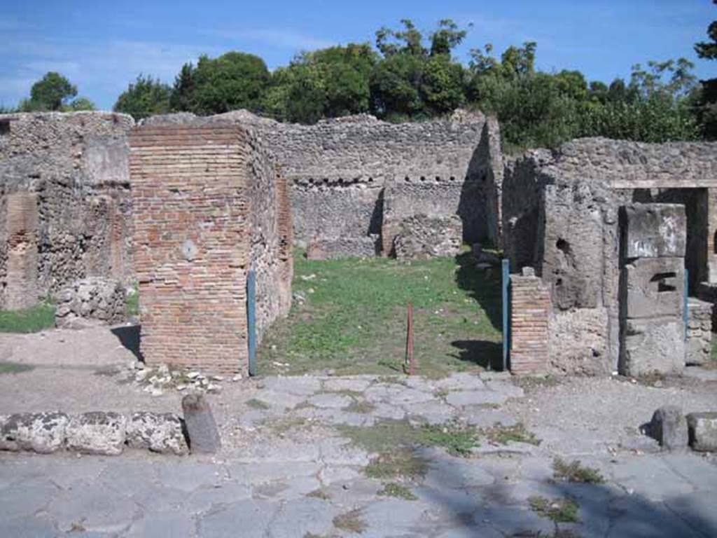 I.1.3 Pompeii. September 2010. Entrance, looking east across Via Stabiana.
Photo courtesy of Drew Baker.
According to Warscher, quoting Mau in Bull. Inst 1875, p.27,  Per lasciar entrare i carri il marciapiede  interrotto avanti alla porta, e il selciato della strada continuato fino allingresso che  largo come quelli delle botteghe ed era chiuso mediante una porta a due partiti. La porta per non si fermava come al solito: nel bel mezzo della soglia di lava vi sono gli avanzi dun uncino di ferro, e pi a sinistra la buca per un chiavistello solo, mentre laltro partito ne stava senza.  Invece al di fuori della porta si trovano nella soglia quattro buche quadrangolari, due vicine ai cardini, le altre m.0,20 discoste da quelle.
See Warscher T., 1936. Codex Topographicus Pompeianus: Regio I.1, I.5. Rome: DAIR, whose copyright it remains (no.12).
(translation:For the carts to enter, the pavement was interrupted in front of the doorway, and the paved roadway continued up to the entrance that was as wide as the doorway of the shops and was closed by means of a door with two entries. The door, however, didn't close as usual: in the middle of the lava threshold there were remains of an iron hook, and more to the left the hole for a latch only, whereas the other entry was without one. Instead outside the door in the threshold were four rectangular holes, two near to the hinges, the others 0,20m distant from those.")
