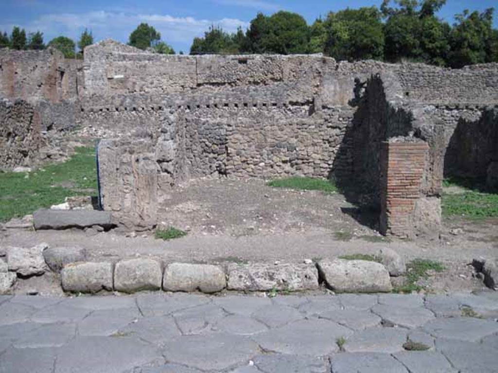 I.1.6 Pompeii. September 2010. Looking east towards entrance on Via Stabiana. Photo courtesy of Drew Baker.

According to Warscher, quoting Mau in Bull.Inst 1875, p.30, I.1.6-9:  Segue un altro albergo, molto simile a questo descritto.  Qui pure  interrotto il marciapiede per lasciar entrare i legni. Lentrata era chiuse mediante una porta a quattro partiti, congiunti a due adue, come si conosce dai quattro buchi per i chiavistelli.  Qui pure si entra prima in un compreso che ha le dimensioni duna bottega grande con una dietrobottega e posteriormente si apre sopra una grande corte, lungo il cui muro di fondo qui pure si stende la stalla, larga 13,30, profonda 2,47 con una finestra sul vico settentrionale e due porte, una allestremit meridionale, laltra poco distante da quella settentrionale. 
Presso a questultima una parte della corte  selciata.   Lungo il muro N vi sono due camere con finestre sul medesimo vico, e prossimo alla stalla il cesso.  Si vede anche il cesso del piano superiore e i tubi di mattone dun terzo, che stava ancora pi in alto.  
Nellangolo NO vi sono I primi gradini duna scala, la cui parte superiore sar stata di legno, in quello SO lapertura della cisterna, e accanto nella stessa massa di materiale una vasca lunga stretta e bassa, come quella sudescritta nella casa adiacente. 
Qui la vediamo frapposto fra la cisterna ed il muro di O, il che esclude categoricamente laver essa servito dabbeveratoio.  Dalla parte pi bassa di essa, aperta come nella casa sudescritta, lacqua colava in unaltra vasca larga 1,02 x 1,54, di cui un lato viene formato dalla suddetta massa di fabbrica, uno dal muro occidentale, i due rimanenti da appositi muricciuoli.   Essa ha al fondo uno scolo verso N, che d in un vaso ossia tubo di mattone, incastrato nel suolo. Nella parete vi era la pittura dei Lari, di cui sono rimasti soltanto i serpi. A destra dellingresso per i legni sta un locale come una bottega. 
Lessere esso congiunto mediante una porta con quel primo compreso, ove entravano i legni, ci lascia supporre, aver esso servito di caupona per i vetturini.
See Warscher T., 1935. Codex Topographicus Pompeianus: Regio I.1/I.5. Rome: DAIR. (no.14)
(translation: I.1.6-9: Followed another hotel, very similar to this.  Here also the pavement was interrupted to allow entry for the carts?/the wood?. The entrance was closed by a door of four entries, joined two by two, as you knew from the four holes for the bolts. Here we entered first into a complex that had the dimensions of a large shop with a rear-room and behind, it opened onto a large courtyard, along whose rear wall was the stable, l3,30 wide,  2,47 deep, with a window onto the northern roadway and two doorways, one at the extreme southern end, the other not far from the north. Near to this last, a part of the courtyard was paved. Along the north wall there were two rooms with windows onto the same roadway, and the toilet was next to the stables.  Also, you could see the toilet on the upper floor and the brick pipes of a third, who was even higher still. In the north-west corner , there were the first steps of a staircase, the upper part would have been of wood, in the south-west was the opening of the cistern, and nearby in the same mass of material there was a long narrow and low basin, the same as that described in the adjacent house. Here we see it came between the cistern and the west wall, which excluded categorically that it was used as a drinking trough. From the lower part of it, open as in the described house, water strained into another large basin 1,02 x 1,54, one side of which was formed by that mass of masonry, one from the western wall, the two remaining from suitable low walls.  It had at the bottom a drain to the north, which went into a jar or brick (terracotta?) pipe, buried in the ground. On the wall there was the painting of the Lares, of which only the serpents remained. To the right of the entrance for the carts, was a room like a shop. This was connected through a door with that first area, where the carts entered, 