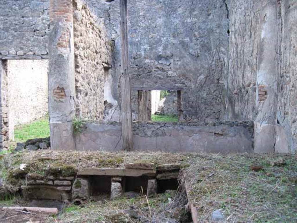 I.2.28 Pompeii. September 2010. Looking south across triclinium towards rear room with window, and doorway to tablinum (on left). Photo courtesy of Drew Baker.
According to Warscher, Il triclinio occupa la parte opccidentale del pseudo-peristilio. 
Si vedono quattro buchi rettangolari che illuminavano il sotterraneo; lingresso a questo ultimo  dalla stanza adiacente (a sinistra nella fotografia no.54 (stanza L).

According to Warscher, quoting Mau in Bull. Inst, 1874, p.250/51, she wrote 
Il peristilio, situate pi alto dell atrio a causa del terreno inuguale, ha corridoi di 3 e 3 colonne sui lati S ed E, mentre verso N ed O confina con le case adiacenti (I.2.17; I.2.22; I.2.24).  Le colonne sono di mattoni e di stucco rozzo, color di carne fino allaltezza del muriciuolo che le congiunge, bianco di sopra. La parte occidentale del portico meridionale, posteriormente soltanto, come ci fa testimonianza lo stucco delle colonne, coperto dal muro, ne fu separato e trasformata in una camera, che mediante una porta corrisponde colla camera a sinistra del tablino, mentre verso N con una finestra larga, distante dal suolo m.1,52, si apre sul peristilio. Sotto il pavimento di questa camera v un cavo, largo m. 0,98 + 0,67, profondo m. 1,32, rivestito di stucco e di sopra a met coperto, mentre lapertura che rimane evidentemente doveva chiudersi con un coperchio. Sifatto cavo, il primo di questa sorta che si sia trovato a Pompei, serviva senza dubbio per conservare tutto ci, che si voleva difendere dal caldo, facendo cos le veci duna piccola cantina. Sul lato meridionale del peristilio vi  ancora un armadio stretto, aperto verso O, ed il cui fondo viene formato dal muro occidentale della camera a destra dellatrio, la quale sporge un poco nel peristilio.
See Warscher T., 1935. Codex Topographicus Pompeianus: Regio I.2. Rome: DAIR, whose copyright it remains.
(translation: "The peristyle, situated higher than the atrium due to the uneven ground, had a walkway of 3 and 3 columns on the south and east sides, while towards the north and west it was bordered with the adjacent homes (I. 2.17; I. 2.22; I. 2.24). The columns were of brick and rough stucco, red-coloured up to a height of a wall that joined them, white above.  As could be seen by the stucco of the columns covered by the wall, the western part of the south portico at the rear only, was separated and transformed into a room, that by means of a door joined with the room to the left of the tablinum, while towards the north, 1,52 m distance from ground,  a large window opened onto the peristyle. Under the floor of this room there was a pit, 0,98m + 0.67 width, 1,32 m deep, faced with stucco and half covered above, while the opening that remained obviously would need to close with a lid. Such a pit, the first of its kind to be found at Pompeii, was undoubtedly to preserve everything, that you wanted to protect from the heat, thus making this the place of a small cellar. On the south side of the peristyle there was still a narrow cupboard, open towards the west, and whose base was formed by the west wall of the room to the right of the atrium, which protruded a little onto the peristyle ".)


