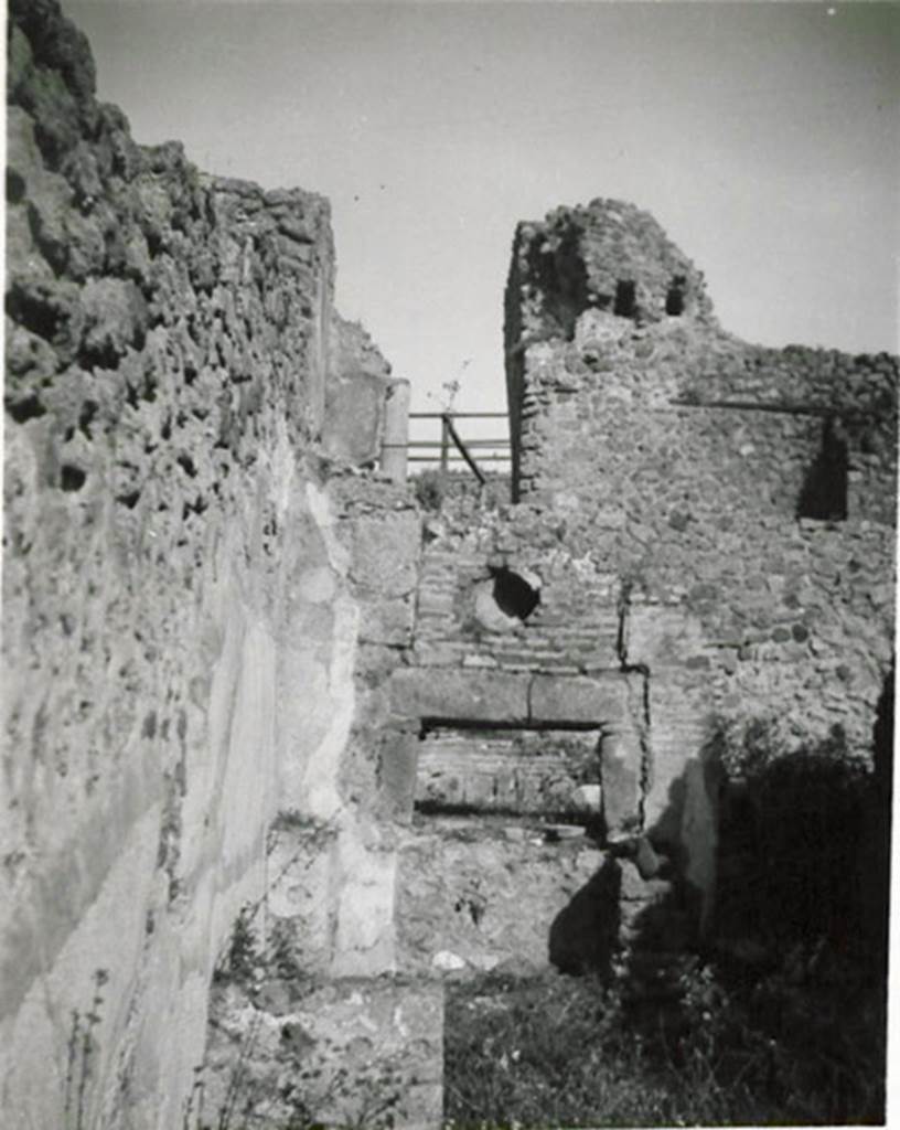 I.3.1 Pompeii. 1935 photograph taken by Tatiana Warscher.
Looking towards oven in north-east corner.
According to Warscher, quoting Fiorelli,  1.3.1. Officina di un pistor dulcarius, che nella taberna prospiciente la via esposti i prodotti lavorati nellattigua cella, la quale prendeva lume dalla bottega, avendone altra pi rozza alle spalle, ed a cui si perveniva passando innanzi al forno; una scala di legno poggiata al muro, ch a sinistra della porta, menava alle stanze superiori. Nel foro per il fumo dello forno  incastrata una cornice di terracotta, forse semplicemente un pezzo di anfora. In fondo si vede il muro con fori di traverse della casa No. 3.
(translation: A workshop of a sweet-pastry maker, that in the shop overlooking the roadway, displayed the products made in the adjacent room, which took its light from the shop, having another rustic room behind, and through which you passed to reach the oven; a wooden ladder rested against the wall, which is to the left of the door, leading to the upper rooms. In the smoke hole in the oven was embedded a terracotta cornice, perhaps simply a piece of amphora. At the rear you see the wall with holes of crossbeams of the house at I.3.3.)
See Warscher T., 1935. Codex Topographicus Pompeianus: Regio I.3. (no.1), Rome: DAIR, whose copyright it remains.

 
