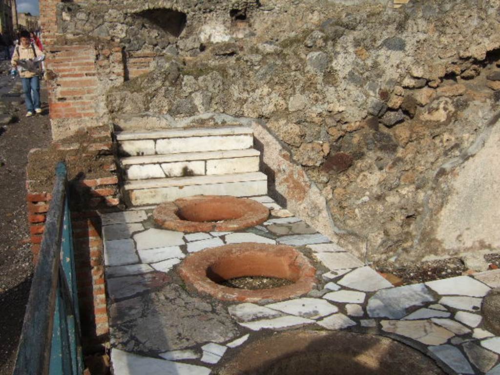 I.3.2 Pompeii. December 2005. 
Looking towards the north wall and counter, with four large terracotta dolia and display shelves. According to Boyce – 
In the north wall is an arched niche (its condition too ruinous for measurement), its walls coated with white stucco.
See Boyce G. K., 1937. Corpus of the Lararia of Pompeii. Rome: MAAR 14. (p.23, no.18). 

