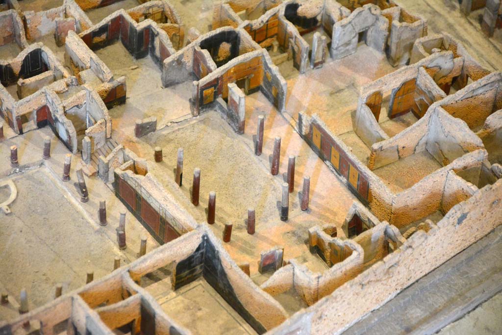 I.4.25 Pompeii. May 2019. Detail from model in Naples Archaeological Museum. 
Looking north-west across upper peristyle 56, in centre, towards open doorway into atrium 47, and through to entrance on Via dell’Abbondanza, centre top.
Foto Tobias Busen, ERC Grant 681269 DÉCOR.

According to Jashemski –
The north (Upper) peristyle garden, which belonged originally to a house whose entrance was on the Via dell’Abbondanza, was reached by a flight of steps from the central (Middle) peristyle which lies on a level about two metres below. This (Upper) garden was surrounded by a portico on the south, east and most of the north sides. There was a travertine puteal between the two middle columns on the east side. On the west, a large exedra (room 57), preceded by a vestibule, had a splendid view of the garden, as did the triclinium (room 58) on the east. The columns, like those in the central peristyle, were made of brick and Sarno limestone and faced with stucco. The columns, with the exception of those opposite the entrances of the large exedra, the triclinium, and to the atrium on the north, were left unfluted. There was a gutter around the edges of the garden.
See Jashemski, W. F., 1993. The Gardens of Pompeii, Volume II: Appendices. New York: Caratzas. (p.31-32).
