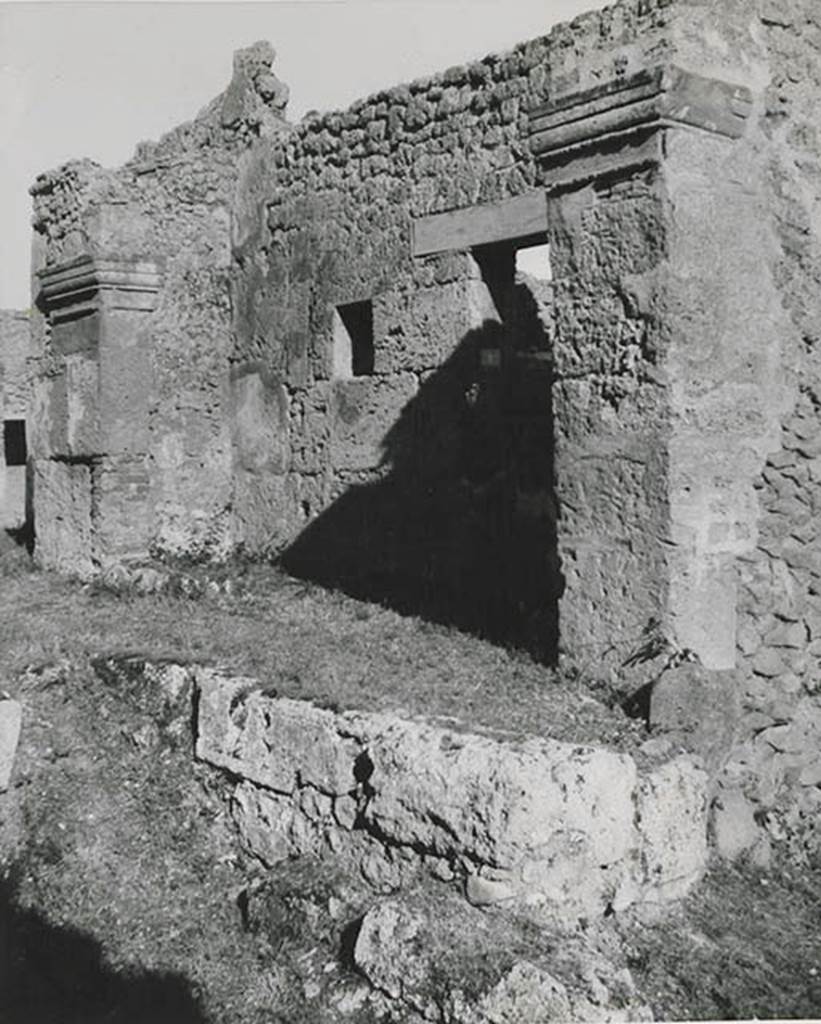 10501-warscher-codex-91-640.jpg
I.5.1 Pompeii. 1936, taken by Tatiana Warscher. 
Looking east along front façade on north side of insula on Vicolo del Conciapelle.

Warscher quoting from Sogliano’s Giorn. Sc. 1874, III, p.8 described –
“I.5.1. Cominciandone la descrizione dal lato settentrionale, incontriamo, a partire dall’angolo nord-ovest, una bottega con piccola abitazione del padrone. Essa è preceduta da una specie di vestibolo, formato da un tettoja, che è sostenuta da un lungo architrave di m. 5,40, poggiato sopra due pilastri finienti con capelli molto semplici. 
La lungezza di questo architrave, che è uno dei più lunghi trovati finora, e l’opus incertum mi fanno credere tale aggiunta molto posteriore all’originaria costruzione della bottega, che sul muro d’ingresso specialmente presenta grosse lastre del tufo di Sarno. Varcata la soglie di pietra vesuviana, munita dei soliti incavi, troviamo sul lato sinistro due cubicoli finestrati, dei quali l’uno è perfettamente rozzo e l’altro avente sulla soglia un cardine di ferro, mostra lievi tracce di una semplicissima decoratione.  Nella bottega sul muro a destra vi è praticato un canale per lo scopo delle acque, e in fondo si trova un dietrobottega.  Credo che il vestibolo suindicato si sia usato per la vendita delle merci.  
Addossata al lato opposto del pilastro sinistro sta un’ara rivestita di stucco con due rialzi arrontodati (arrotondati) al di sopra”.

 (translation: “beginning the description from the north side, we meet in the north-west corner, a shop with small house of the master.  It is preceded by a vestibule, formed with a roof, which was backed by a long lintel (architrave) of 5.40m, resting above two pilasters finished with simple capitals. The length of this lintel, which was one of the longest so far found, and the opus incertum makes me believe that this goes back to the original construction of the shop, which shows big slabs of Sarno tufa on the entrance wall. Crossing the threshold of vesuvian stone, furnished with the usual notches, we find two windowed cubiculums on the left side, of which one is completely rough and the other had an iron hinge on the threshold (doorstep), showing faint traces of a simple decoration. On the wall on the right of the shop, there was a channel for the purpose of water, and at the back we find a rear room. I think the vestibule above was used for the sale of goods. Backing onto the opposite side of the left pilaster was an altar covered in stucco, with two rounded prominences above". )    

From Mau, in Bull. Inst, 1875, p.25, she quoted –
“Sono perfettamente d’accordo coll’autore della descrizione del G.Sc. nell’attribuire ad’un’epoca relativamente recente quel singolare vestibolo che sta avanti all’ingresso della detta bottega”.

(translation: I agree with the author of the description  in G. Sc. in the attribute of a relatively recent time to that singular vestibule which stands in front of the entrance to the said shop).
See Warscher T., 1936. Codex Topographicus Pompeianus: Regio I.1, I.5. (no.16), Rome: DAIR, whose copyright it remains.


