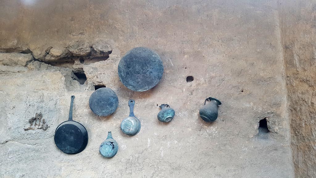 I.6.7 Pompeii. August 2023. Household utensils displayed on south wall of kitchen area. Photo courtesy of Maribel Velasco.
