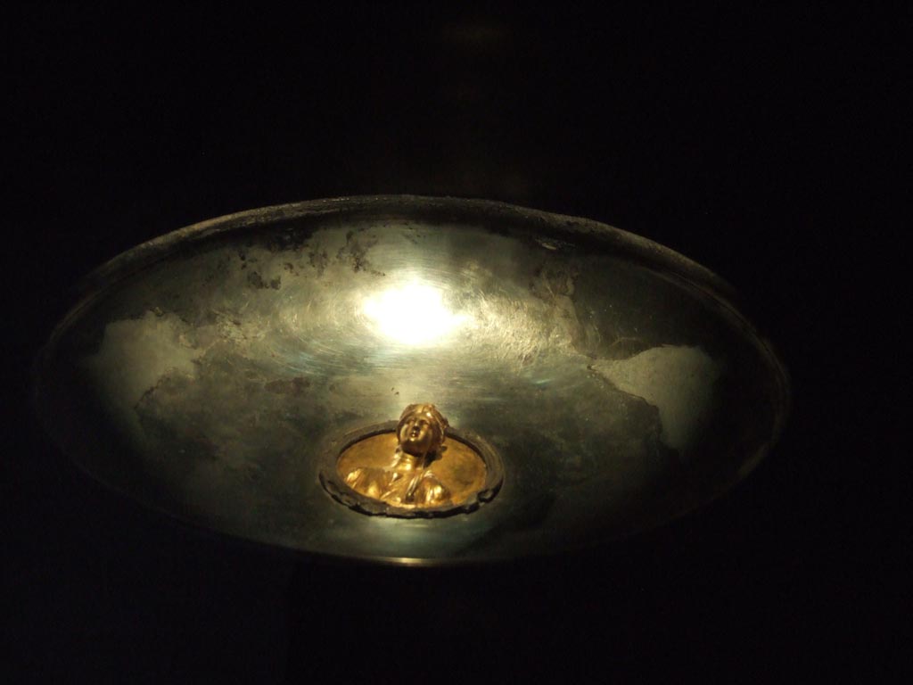 I.10.4 Pompeii. Silver phiale or flat drinking vessel with gold emblem in centre. 
The cup appears to have been used for display and a stand for this was found also.
Part of the 115 pieces of Silver found in a chest in the underground storerooms. 
Now in Naples Archaeological Museum. Inventory number 145544.
See Guzzo, P. (A cura di), 2006. Argenti a Pompei. Milano, Electa. p.220-1.
