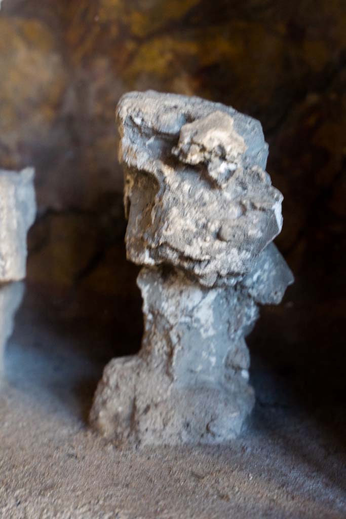 I.10.4 Pompeii. April 2022. 
Alcove 25, detail of plaster cast, seen on the left of centre, on the lararium or domestic shrine. (Image 1).
Photo courtesy of Johannes Eber.
