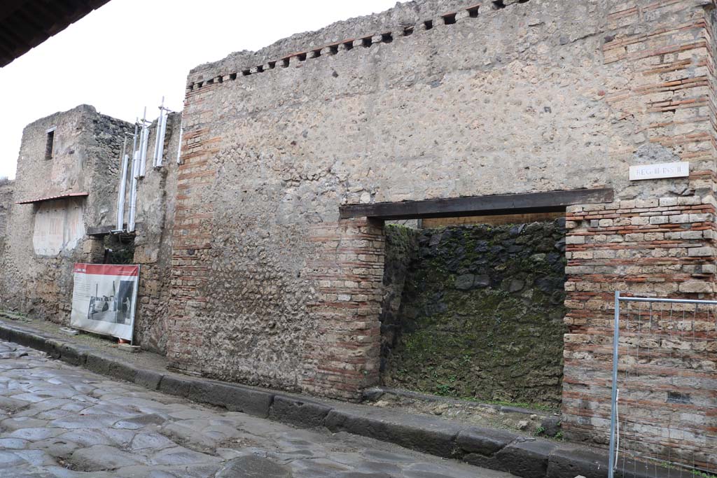 III.2.2 Pompeii. April 2019. Looking towards entrance to shop on north side of Via dellAbbondanza.
The display board, advertising the Temple of Apollo, is a temporary screen.
The Temple of Apollo is to be found in Reg.VII.7.32, on the west side of the Forum.
Photo courtesy of Rick Bauer.
