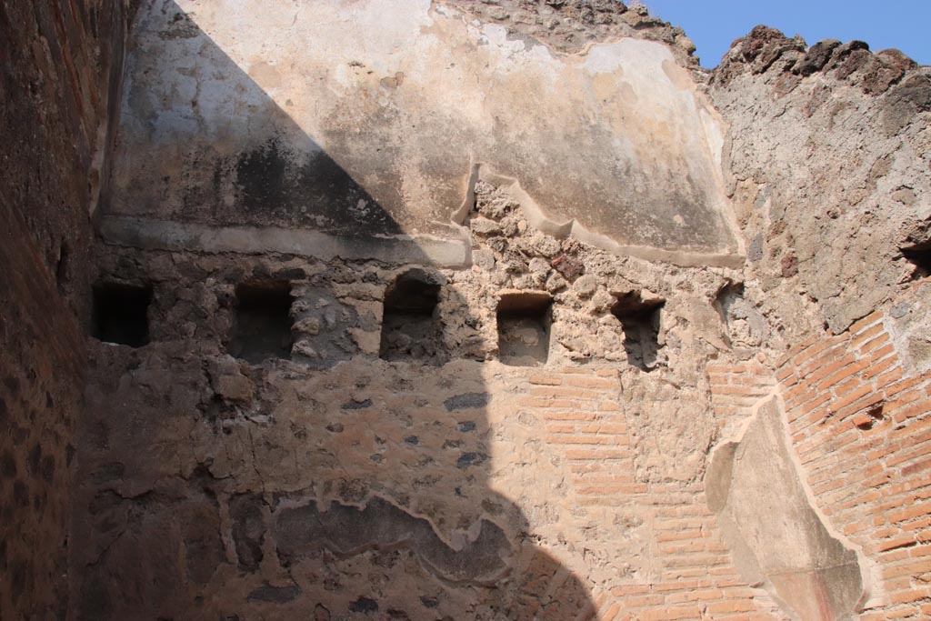 V.1.2 Pompeii. October 2023. 
North wall of kitchen/latrine in north-west corner, with holes for support beams for an upper floor.
The upper room has remaining stucco on its north wall. Photo courtesy of Klaus Heese.
