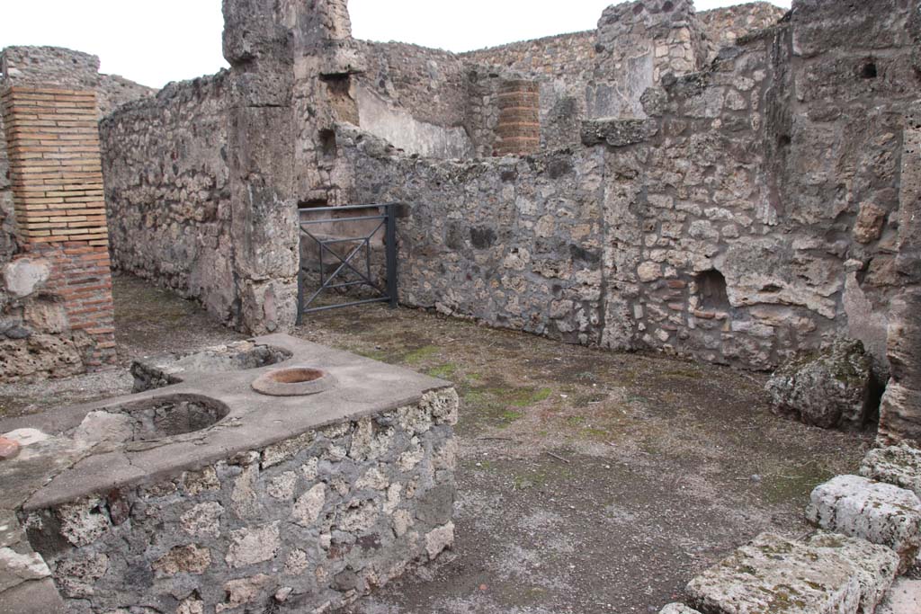 V.1.13 Pompeii. October 2020. Looking towards south side of bar-room, with doorway to rear room, and corridor with arched lararium niche in south wall.
Photo courtesy of Klaus Heese.
