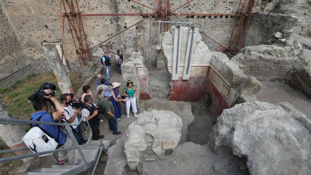 V.2.Pompeii. Casa di Orione. August 2018. 
Looking north towards room A10, a triclinium (upper right of photo). 
This room was the largest of the house, rectangular in shape.
Numerous traces of burnt wood were discovered here in the lapilli, and signs of a fire can be seen on the decoration of the east wall.
See Osanna M, 2019. Pompei. Il tempo ritrovato. Le Nuove Scoperte. Milano: Rizzoli (p. 106). 
In the centre is room A6, garden area 11c is on the left, and portico A19 is full of people.  
Room A18, north ala, is on the centre right.
Photograph © Parco Archeologico di Pompei.


