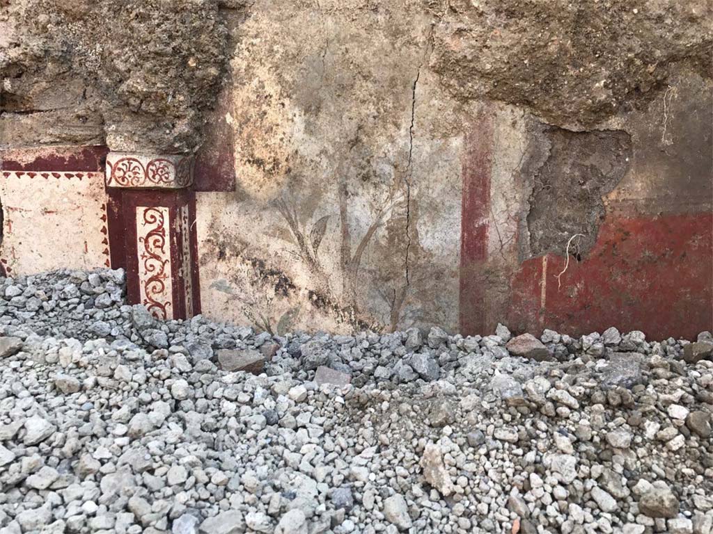 V.3.13 Pompeii. 2018. Room 2a. East wall. A sumptuous painted lararium begins to emerge from the lapilli in a room which was being excavated. 
On the left is the edge of the niche and right is painting of flowers.

Parete est. Un sontuoso larario dipinto inizia ad emergere dai lapilli in una stanza che è stata scavata. 
A sinistra è il bordo della nicchia e a destra è dipinto di fiori.

Photograph © Parco Archeologico di Pompei.

