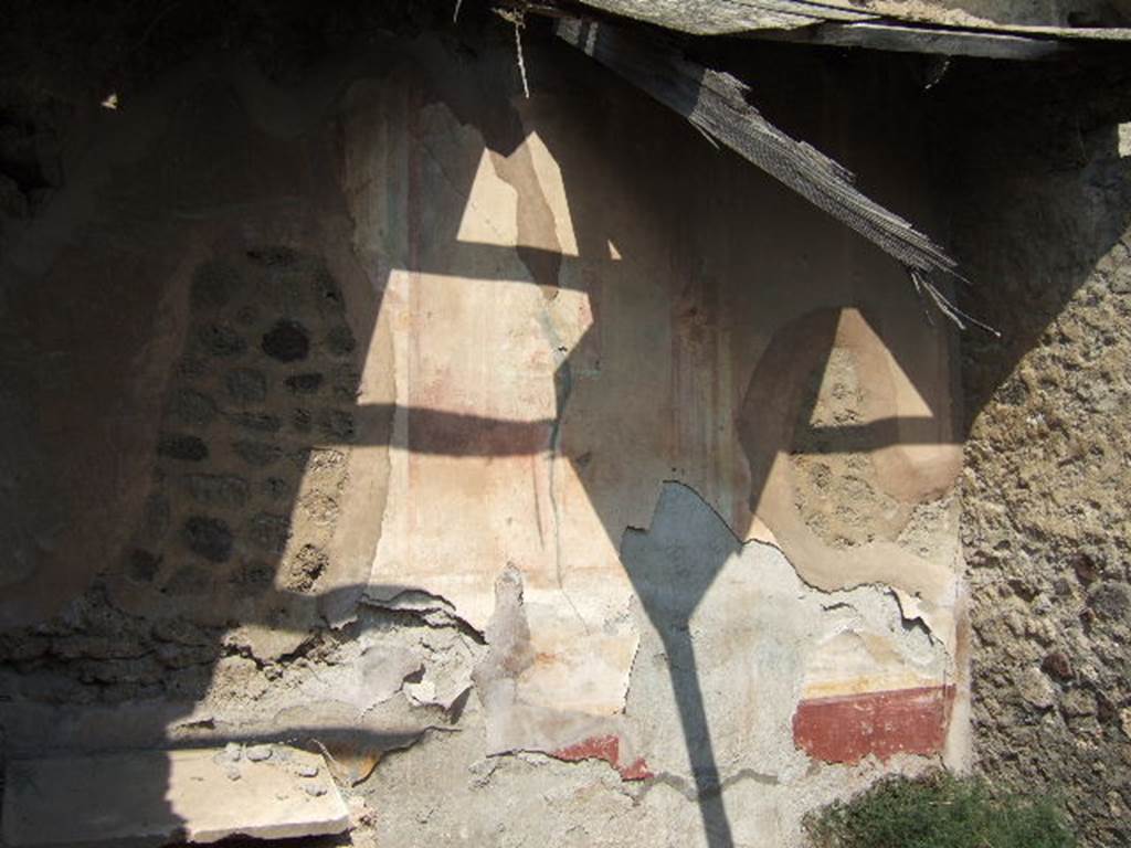 VI.5.7 Pompeii. September 2005. Remains of painted plaster in cubiculum nearest the north-east corner. The zoccolo would have had alternating panels of plants on a red background, and then narrow compartments with painted imitation marble. Above the zoccolo was a green painted predella, with a still-life at its centre. In the centre of the wall would have been a wide yellow aedicula painted with surrounding architectural columns.
