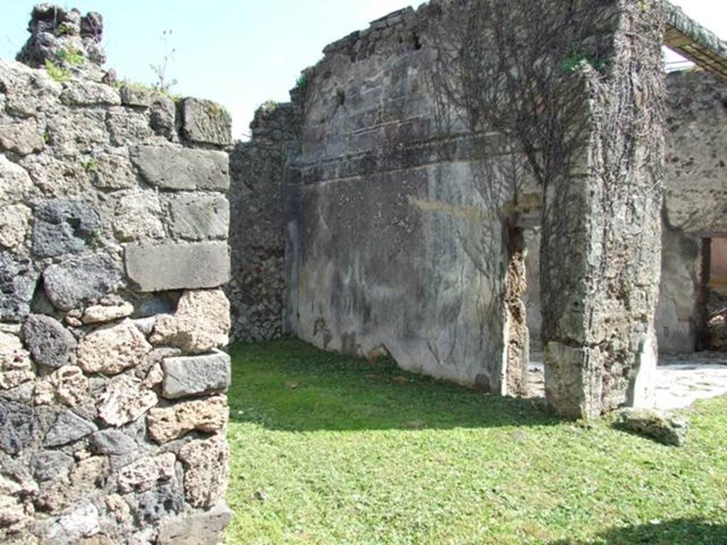 VI.15.5 Pompeii. March 2009. Doorway to room 24, oecus. South wall, with small door into tablinum. According to NdS, this room was a cubiculum and had a floor (alla veneziana) and was decorated in the First Style. On the south wall was the remaining decoration of a previous time showing stucco ashlars. Afterwards, a decoration of yellow panels divided by white areas with candelabra was substituted. The dado was on a black background with the usual concepts of marsh plants. See Notizie degli Scavi, January 1897, (p.27)
