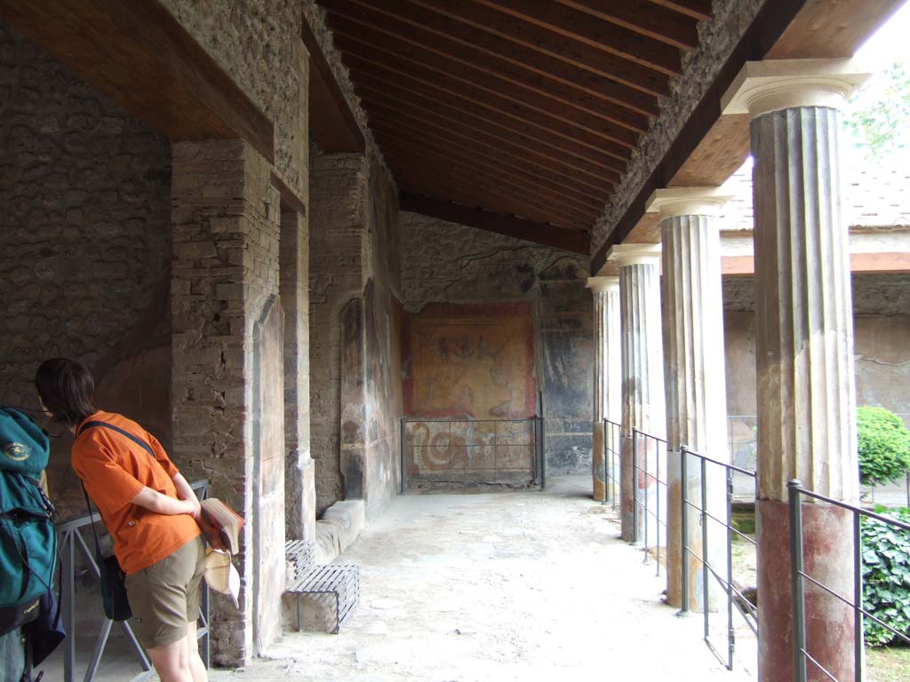 VI.16.7 Pompeii. May 2006. Room F, east portico.  Looking south towards the lararium. 
Nearest on the east wall is the doorway to room G.
Next is the entrance to the long, tall, narrow area 01 with metal steps.  
This had the stairs to the upper floor over room G and the shop at VI.16.6.  
The third entrance with a stone sill is the open area 03 that contained a cupboard.
