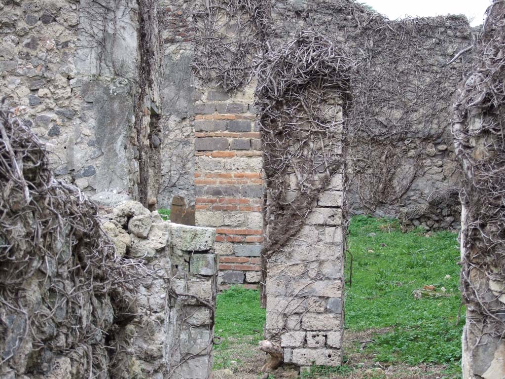 VI.16.10 Pompeii. December 2007. Looking west from triclinium, or cubiculum, across towards rear of house into garden, F.
The pillar, centre left, would have been on the right side of the entrance to the garden area.
It was made of brick and tufa-stone cut into bricks, which were very robust, having to support a roof in F.
The outdoor area F was found with the remains of II style decoration on the north and west walls.
To the left of the brick and tufa pillar, a doorway can be seen. This would have led to the kitchen and latrine.
The other pillar, centre of photo, would have been the one on the north side of the doorway from the corridor. 
