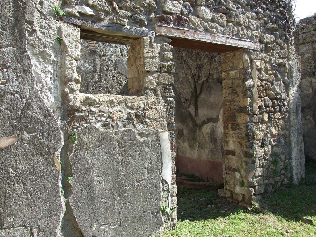 VII.3.30 Pompeii. March 2009. Doorway to room 7, cubiculum.
The south wall of the cubiculum can be seen with a viola zoccolo/dado, above this the wall was divided into two panels in which a central compartment bordered by narrow viola bands/ribbons, and was crossed by a thin yellow painted candelabra separating the side panels with carpet borders with stripes of green and yellow and simple lotuses.
