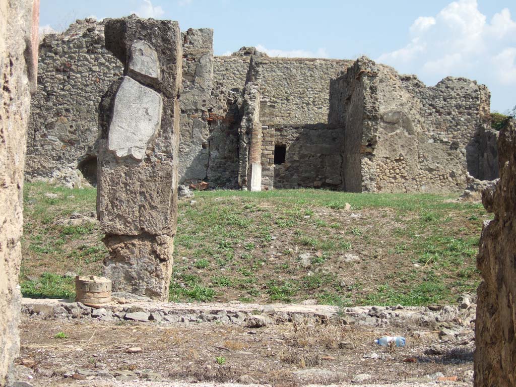 VII.6.38 Pompeii. September 2005. 
Looking east across portico towards site of exedra/oecus or tablinum, in lower centre, and VII.6.28 in the background.
According to NdS (1910) -
“On the eastern portico of the peristyle, Exedra 23 opened in all its width, spacious and elegant, with two columns, between the jambs (once covered with wood) which supported the architrave. The room was therefore not closed by shutters, and the doorway lacked a threshold, whose place was occupied by the same flooring as the whole room, formed of cocciopesto with pieces of various coloured marble, inlaid here and there. 

The square-shaped room was divided from the side rooms only by thin walls, now fallen, and bore a beautiful painted decoration, now preserved only at the bottom of the facing wall. From this little we see, that the wall showed three large rectangles, the central red and the sides yellow, divided by wide bands probably black, and lower however purple/peacock blue, showing perhaps fantastic architectures, and leaning (what you can see) on two pedestals, each consisting of a forepart of the general zoccolo of the wall.  This zoccolo/plinth was black with a purple/peacock blue squaring in the central area, and purple/peacock blue with black squaring in the side areas.  Of these three panels, the first one showed a very damaged mask in prospect, perhaps of a female with a kind of pine on top, from which two swirls of floral scrolls come out, all yellow. Each of the other two showed a dolphin. Under this zoccolo was another lesser painting in imitation of slabs of inlaid coloured marble.

In the south wall, today as I have said, destroyed, would have been two doorways, which gave access to small rooms 25 and 26.”
See Notizie degli Scavi di Antichità, 1910, p.446-453.
