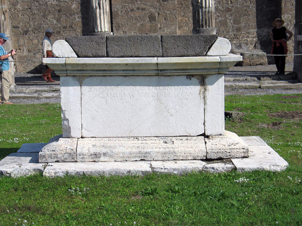 VII.7.32 Pompeii. October 2005. A view of the west side of the altar in front of the Temple of Apollo at Pompeii.
The inscription (visible just underneath the shadow) reads:
M. PORCIVS. M. F. L. SEXTILIVS L.F. CN. CORNELIVS. CN. F
A. CORNELIVS A. F. IIII. VIR(i). D(e). D(ecurionum). S(ententia). F(aciundum). LOCAR(unt)
According to Roger Ulrich, the use of the term quattuorviri (designated by the Roman numeral IIII) appears after the (re)foundation of Pompeii as a Roman colony for the veterans of Sulla in 80 BCE.
It thus sets a date limit after which the inscription was made.
The best known of the Pompeians named was M. Porcius, who was also a patron of the Theatrum Tectum (small covered theatre or Odeon) and the Amphitheatre.
The altar has a base of travertine, more expensive marble sides (imported from Greece?) and a table top of lava stones.
Photo Courtesy of Roger B. Ulrich.
