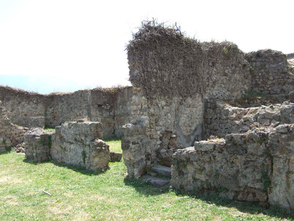 VII.12.3 Pompeii. May 2006. Rooms on west side of atrium.
According to Eschebach, on the right side of the atrium were steps to the upper floor, these are on the right of the photo above.
On the left of the photo, there was a windowed triclinium with a wide opening onto the north portico of the garden.
Also, on the right was a lararium.
See Eschebach, L., 1993. Gebäudeverzeichnis und Stadtplan der antiken Stadt Pompeji. Köln: Böhlau. (p.326)
According to Boyce, on the west side of the atrium Fiorelli reported a larario; but now there only remains a ruined brick base.
This may have supported an aedicula.
See Boyce G. K., 1937. Corpus of the Lararia of Pompeii. Rome: MAAR 14. (p.70, no.312). 
