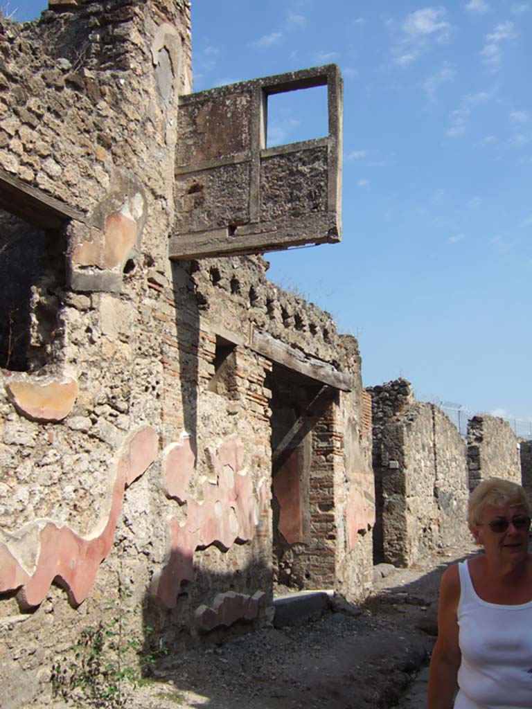 VII.15.5 Pompeii. September 2005. Looking east to entrance doorway, with holes above for support beams of balcony.
As these were recognised at the time of the excavation, this allowed for the reconstruction of the projection. 
The exterior walls were covered with painted stucco decorated with large red panels bordered by “yellow carpet edging”, and above were yellow bands, whose colour, because of the heat of the eruption products, had become red.
