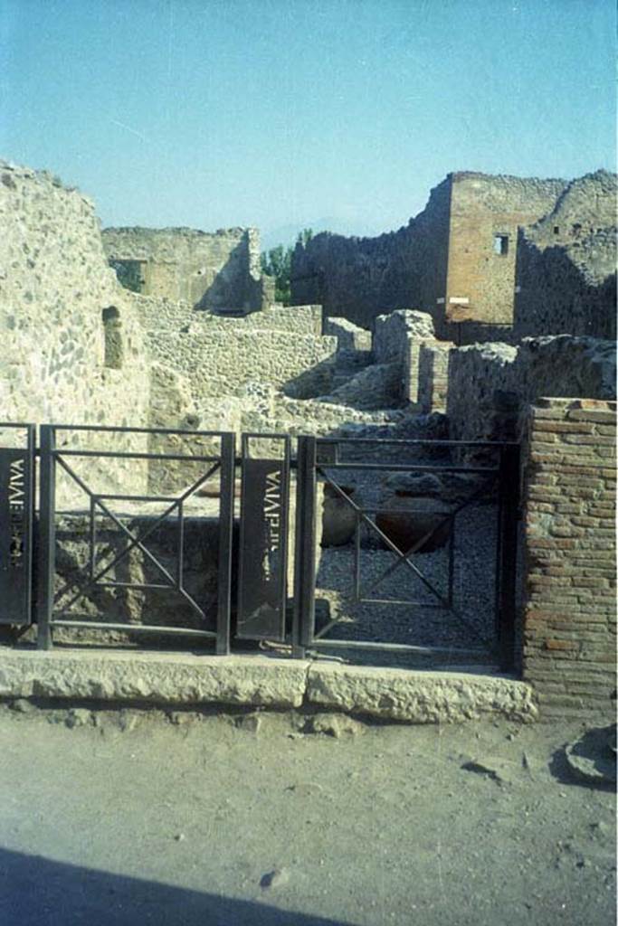 VII.16.7 Pompeii. July 2011. Entrance doorway. Photo courtesy of Rick Bauer.
According to Fiorelli -
“Questa bottega tiene sul pilastro che la precede un’edicola di fabbrica, ed in essa una pelta marmorea, con rilievo di due maschere tragiche e due faci, gia servita a decorare l’intercolunnio del portico di qualche ricca abitazione, e poi posta qui come segno averrunco contro il fascino. Al di sotto dell’edicola era dipinto:
CASELLIUM.AED.OVF
Essa probabilmente fu un termopolio, standovi il podio con due urne ed i consueti gradini per le stoviglie, il focolare, due nicchie per i Penati, ed una cella nel fondo con uscita nel vico orientale no.8.”
See Pappalardo, U., 2001. La Descrizione di Pompei per Giuseppe Fiorelli (1875). Napoli: Massa Editore. (p.161)
(translation: This shop had a masonry aedicula on the pilaster that preceeded it, and in it was a marble pelta with the relief showing two tragic masks and two faces, formerly used to decorate the intercolumniation of the portico of some rich house, and then placed here as a sign against the evil-eye. Painted underneath the aedicula was
CASELLIUM.AED.OVF
It was probably a thermopolium, because of the podium with two urns and the usual steps/shelving for the crockery, the hearth, two niches for the Penates, and a room at the rear with another exit at VII.16.8 in the eastern vicolo.”)
