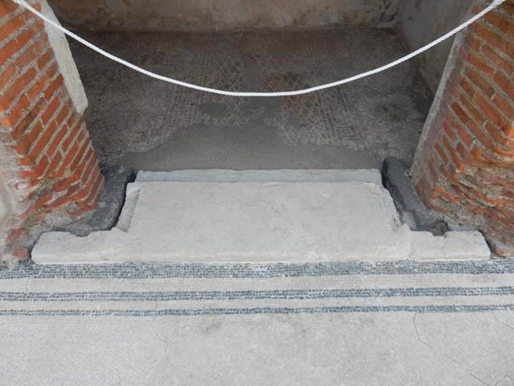 VIII.2.16 Pompeii. May 2017.  Threshold to doorway of cubiculum in centre of south wall of atrium. Photo courtesy of Buzz Ferebee.
The indents in the limestone threshold clearly show that the doorway was fitted with wooden door-jambs and that its doors opened inside the room, where the floor decoration clearly defined the anticamera and the bed alcove. The floor is seen with a “carpet” outline of white tesserae in a diamond shaped net design with a border of meanders alternating with squares and a central tessera.

