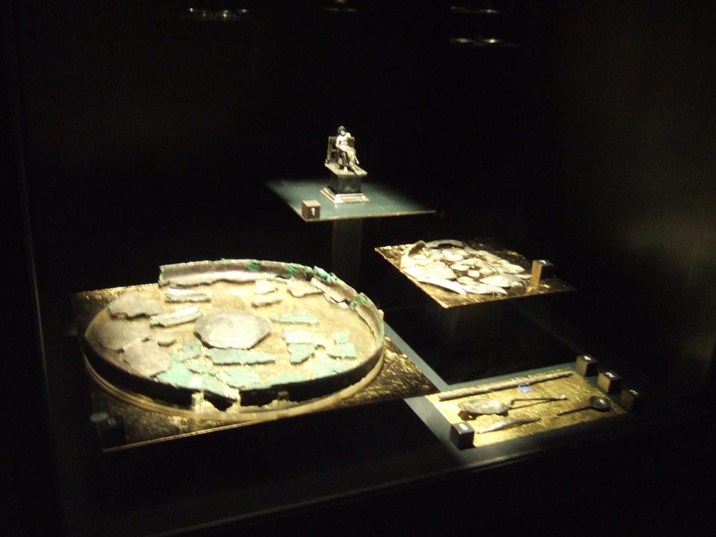 Silver found 20th September 1887 in VIII.2.23. Now in Naples Archaeological Museum.
Statuette of Giove seated on a throne (rear).  Inventory number 116356.
Centre left is the remains of a silver tray. Inventory number 116363.
Centre right is the remains of a silver plate. Inventory number s.n.
Bottom right is a group of four silver items.
See Guzzo, P. (A cura di), 2006. Argenti a Pompei. Milano, Electa. (p. 134).
