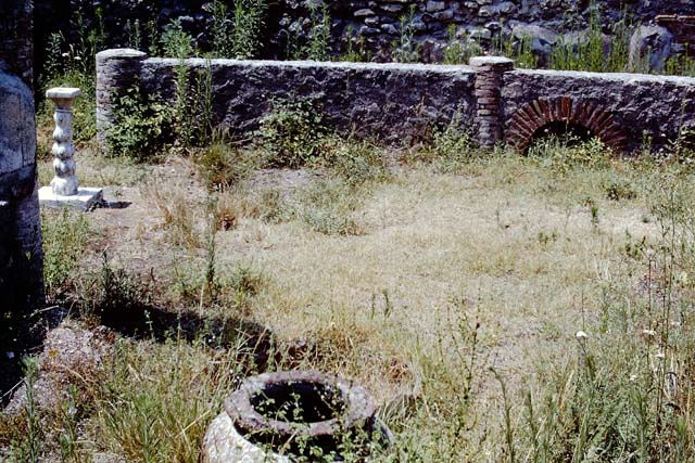 VIII.4.12 Pompeii. December 2018. 
Detail of large stone used as base for an arca, near south wall of peristyle. Photo courtesy of Aude Durand.
Description by Niccolini, but see also VII.2.18 –
12/13. Shops, from one of which one enters into an atrium with two rooms on the left, of which one used as a cupboard was next to the steps to the upper rooms, very worn out by use: then comes a corridor with the kitchen on one side and the store-cupboard on the other, and then follows an area surrounded by a portico, under which there are two other rooms, a cupboard, a repository, and in front of the aforementioned corridor two spacious triclinia, with an adjacent room: leaning against the pillar that divided the entrance doorways of the two triclinia was the iron arca (money-chest). In the area, seven dolia, a marble monopodium and a masonry basin are buried in the soil.
See Niccolini F, 1862. Le case ed i monumenti di Pompei: Volume Secondo. Napoli, (Descrizione Generale, p. 67, and Tav. XXXIII below).
