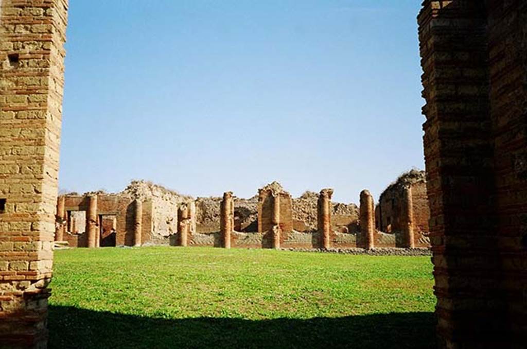 IX.4.5 Pompeii. October 2009. Looking east from entrance across palaestra “d”.
Photo courtesy of Rick Bauer.
The window and door on the far left side is the apodyterium or vestibule “i”, leading to possible shops “k”, “l”, “m”, “n” and “o”.
The next three windows in the centre are the apodyterium or frigidarium “p”.
The three windows on the left are the tepidarium “q”.
The taller building on the extreme right is the caldarium “s”.
