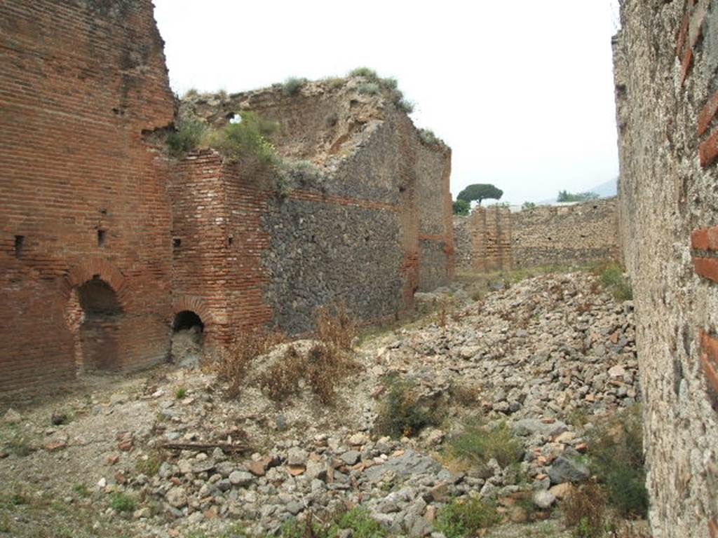 IX.4.15 Pompeii. May 2005. Looking north from entrance into area t. The exterior wall of the laconicum (sweating room) r can be seen in the centre of the picture. Three pilasters can be seen to the north of the wall in open area u. According to Mau
Between the rooms of the Baths and the eastern vicolo, there was only an area of open space, accessible by the two doorways from the eastern vicolo, and from which by a corridor you would pass into the vestibule [i].  In the northern part are 3 pilasters of brick and limestone cut to look like masonry bricks, and it seems that they should have supported a roof  that in the guise of a portico would have covered the north side, and a part of the west side. See BdI, 1878, (p253 of pages 251- 254). 
