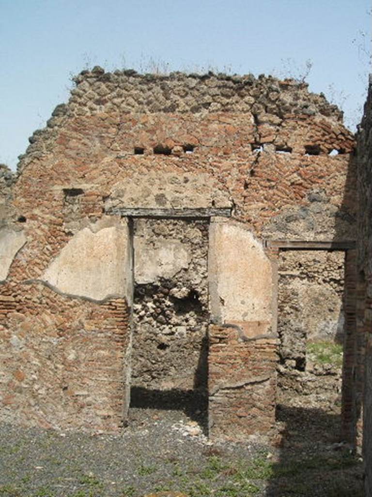 IX.6.3 Pompeii. May 2005. Doorways to two rooms “c” and “d” on north side of atrium.
The small square window of room “c”, placed very high which faced onto the atrium, can be seen on the left. This was probably the bedroom of the owner, and it was his seal that was found here with the letters P.F.L. Also found here were a bronze lantern, a weight, a measuring jar, a necklace of 21 vitreous paste globes, and three marble mortars (Notizie 1879, p.154, 29th March). The walls had badly preserved decoration and of no value, executed in the IV style. In the moon-shape of the decorative vault, opposite the entrance doorway, was seen a large painted peacock that was going to the left towards a fruit, which was between low plants on the earth. To the right of the entrance was a square window placed very high, which faced onto the atrium. The doorway was without a threshold; the hinges were fixed onto two marble slabs stuck in the floor below the door jambs. Recesses were missing for the bolts; instead the inside of the door could be closed with a cross beam inserted into two holes visible in the jambs.At a distance of around 1,0 out from the door was a rough hole in the floor, and it seemed that this also served to close the door using a beam placed obliquely, with one end in that hole, with the other against the door.
