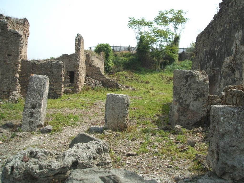 IX.6.4 Pompeii. May 2005. Looking east across site. The eastern extent of the house can be seen across the centre of the photo, in the middle left. The pile of stones in the middle centre of the picture, against the north-east wall of the kitchen, would be the site of the hearth, with site of lararium painting above it.  The wall with a doorway in room “z”, leading to the peristyle of IX.6.5, can be seen in the wall on the left. According to Garcia y Garcia, during the night bombing of 16th September 1943, the prothyron, the atrium and four nearby rooms adjoining the south and south-west of this house, were hit by a bomb. Also the pavement and street outside were damaged. Another bomb destroyed a good part of the large room on the east of the house and the perimeter eastern wall of the room on the north-east.
See Garcia y Garcia, L., 2006. Danni di guerra a Pompei. Rome: L’Erma di Bretschneider. (p.153)

