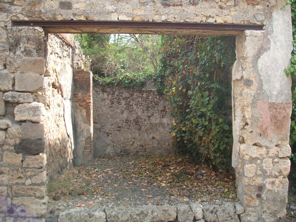 IX.7.18 Pompeii. May 2005. Entrance, looking east across the shop towards the area of a rear room.
According to Mau, the rear room (room e in IX.7.19) was a cubiculum.
He also stated that he thought originally in ancient times the shop, at the front of the photo, would have been closed from the street.  
The shop is also described as room “d” in IX.7.19.
The doorsteps of both doorways, IX.7.18 and IX.7.19 were missing when excavated.
It was not known what items were sold in the shop whose walls were covered with white stucco.
Above the entrance, Mau could see a red band which was the remains of a decoration from the 1st style.
See Bullettino dell’Instituto di Corrispondenza Archeologica (DAIR), p.78-9
