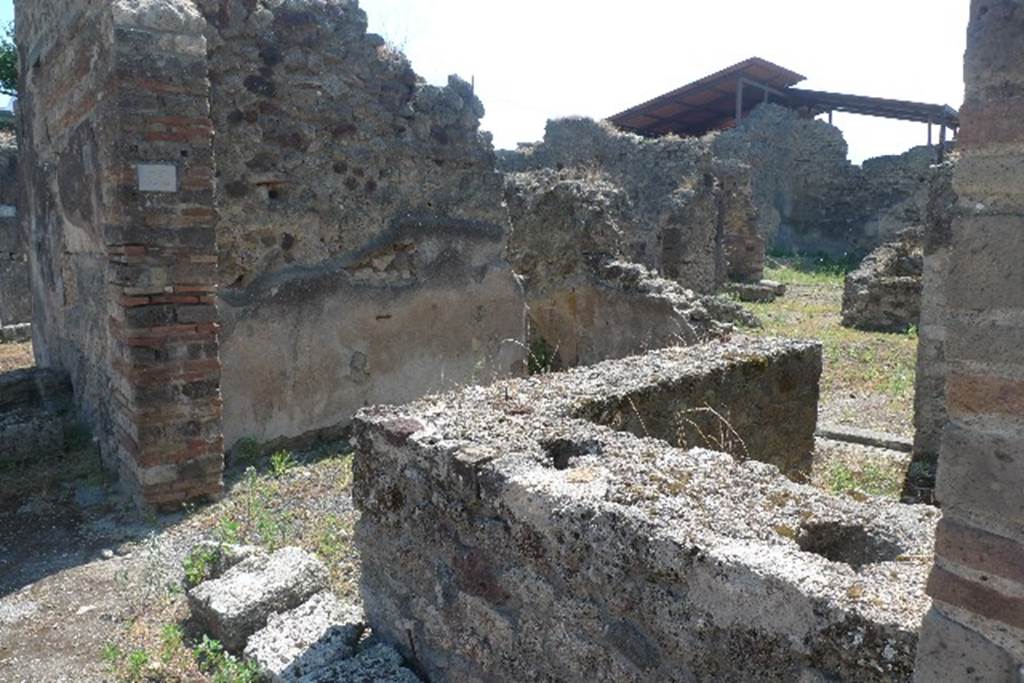 IX.7.22 Pompeii. July 2010. Looking south-east across remains of counter. 
Photo courtesy of Michael Binns.
According to Mau, the podium was covered in stucco, red at the front, and rough and reddish at the rear.
The top had been covered with slabs of marble, which were missing.
On the 30th October 1880, six amphorae with inscriptions were found here.
Also found was a broken amphora containing some lentils.
On the 4th February 1881, in the presence of Granduca Nichola di Russia, were found: 
 The base of an amphora with unidentifiable burnt material.
 A terracotta lamp 
 3 glass bottles and fragments of a fourth
 Part of the bronze fittings of a chest
 An iron hoe, 11 iron keys and small iron anvil
 2 bone dies (for game of dice) 
 A glass-paste amulet representing a small herm. 
See Notizie degli Scavi di Antichit, 1880, p.400, 1881, p. 61-2.
See Mau in BdI, 1882, p. 193.
