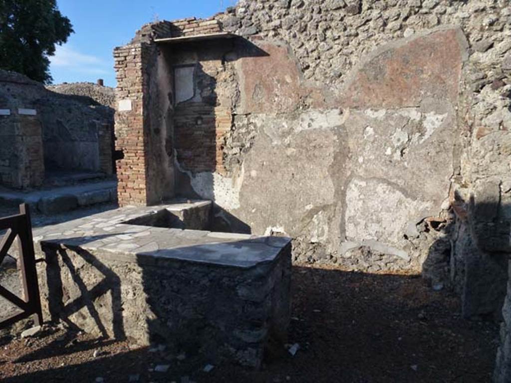 IX.9.8 Pompeii. June 2012. Looking east across bar and counter. Photo courtesy of Michael Binns.
According to NdS, the usual sales-counter was situated near the entrance to the bar.
On the east wall was a painting of a gladiator, (the part that remained being 60 high x 50 wide) which had been covered over and a new layer of plaster applied on top.
When the upper layer fell, the painting reappeared on a white background.
The figure of the gladiator was armed with a crested helmet with perforated visor, a large, curved rectangular shield, and legging on his left leg.
Near his head the following inscription in black letters was read 
AEDIM  SVLL   XLIX         
        V                               [CIL IV 3789]
See Notizie degli Scavi, 1889, p.126, (note the difference between XLIX above, and Soglianos XIIX below).

According to Jacobelli, Sogliano thought that AEDIM was what remained of the gladiators name.
His armour indicated that he was a Samnite.
XIIX was the number of contests that he had fought, and the letter V meant he was victorious in that particular contest.
SVLL showed that he belonged to the family Sullana.
See Jacobelli, L., 2003. Gladiators at Pompeii. Rome: LErma di Bretschneider. 

According to Epigraphik-Datenbank Clauss/Slaby (See www.manfredclauss.de) this read

]aedim(us?) Sull(anus?) XIIX 
V      [CIL IV 3789]
