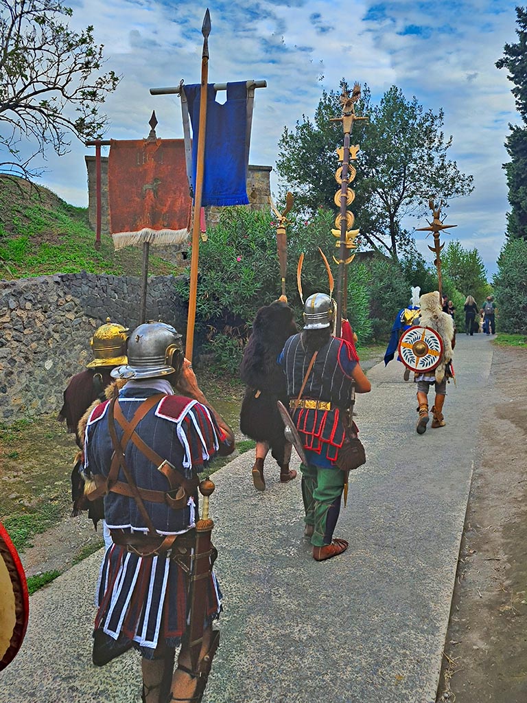 Vicolo dell’Anfiteatro between II.5 and II.4. September 2024. 
Legionary standard bearers marching to amphitheatre.
Looking south during “Ludi Pompeiani” event. Photo courtesy of Giuseppe Ciaramella.

