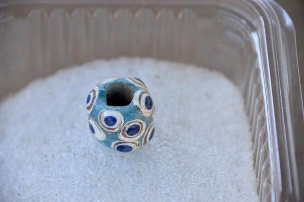 Santuario extraurbano del Fondo Iozzino. 2014 excavations.  A turquoise bead decorated with gold, white and blue ringed patterns.

Una perla turchese decorata con motivi ad anello oro, bianco e blu.

Photograph © Parco Archeologico di Pompei.


