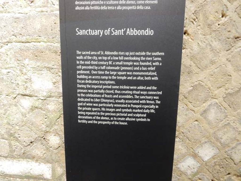 Tempio dionisiaco in località Sant’Abbondio di Pompei. May 2018. Antiquarium exhibition description of the temple.
According to the Parco Archeologico di Pompei, it is located just outside the city walls on top of a low hill overlooking the river Sarno.
A small temple was founded in the 3rd century BC with a cella preceded by a tufa colonnade (pronaos) and the low relied pediment. 
Over time the large square was monumentalised, building an access ramp to the temple and an altar, both with Oscan dedicatory inscriptions.
Some triclinia were added in the Imperial period and the pronaos partly closed creating ritual ways connected to the celebration of feasts and assemblies.
The sanctuary was dedicated to Liber (Dionysus), usually associated with Venus.
The god of wine was particularly venerated in Pompeii especially in the private spaces.
His images and symbols marked daily life, being repeated in the precious pictorial and sculptural decorations of the domus, so as to create allusive symbols to fertility and the prosperity of the house.
Photo courtesy of Buzz Ferebee.
