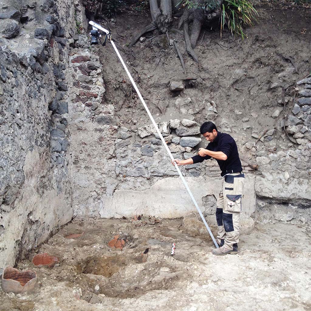 HGE28 Pompeii. 2014. Bastien Lemaire photographs the locations of potters wheels using a pole. Photo  Guilhem Chapelin.
According to Laetitia Cavassa, after removing the modern rubble, four circular cavities were unearthed, three of whose walls consisted of fragments of cut amphoras; these were the remains of the potters wheels. This was a major discovery, as it illustrated through archaeological remains what we already knew, but only with regard to frescoes. Among the rare representations from the Roman period illustrating potters wheels at work, two are mural paintings discovered in Pompeii. Now we have these Pompeian wheels. While these traces are fleeting, they indicate the location of the master turners as well as the how these wheels worked. We noted the presence of a central axis made of wood on which the turning wheel was placed. The entire chain of operation has now been illustrated, from the shaping of vases, unfired goblets, and the firing of vases in kilns. 
See Laetitia Cavassa, 2019. Tracing Back the Potters of Pompeii.  Article in English

HGE28 Pompeii. 2014. Bastien Lemaire photographie les emplacements des tours de potiers  laide dune perche. Photo  Guilhem Chapelin.
Rapidement, aprs avoir enlev les dblais modernes, nous mettons au jour quatre cavits circulaires dont la paroi est constitue, pour trois dentre elles, par des fragments damphores tailles : il sagit des vestiges des tours de potiers dont nous cherchions les emplacements. Nous les avons enfin trouvs.
La dcouverte est de taille : elle vient illustrer par des traces archologiques ce que nous ne connaissions jusqualors que par des fresques. Parmi les rares reprsentations dpoque romaine illustrant des potiers en train de travailler, deux sont des peintures murales dcouvertes  Pompi. Maintenant, nous avons les tours pompiens. Ces traces, bien que fugaces, indiquent la position des matres-tourneurs ainsi que le fonctionnement de ces tours de potiers. On constate la prsence dun axe central en bois sur lequel tait place la roue du tour. Toute la chane opratoire est dsormais illustre, de la mise en forme des vases, en passant par les gobelets crus, jusqu la cuisson des vases dans les fours.
Voir Laetitia Cavassa, 2019. Sur la trace des potiers de Pompi.   Article en franais 
