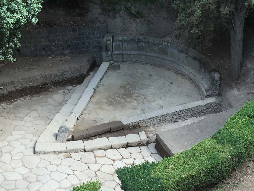 NGH Pompeii. 2015. Schola tomb after clearance showing previously covered tomb and basalt block roads. 
The continuation of ancient Via di Nola into unexcavated area is on the left.
The area immediately outside of Porta Nola (the Nolan Gate) was first cleared in 19078. 
Since then, soil had once again accumulated opposite the gate, re-burying the tomb. 
In 2015 the Porta Nola Project has cleared the basalt block roads and brought the monument back to light.
Excavation inside the monument in front of the benches revealed a thick layer of floor preparation for the pavement which has since disappeared.
See BSR Pompeii Project Porta Nola Necropolis 2015 Excavations
