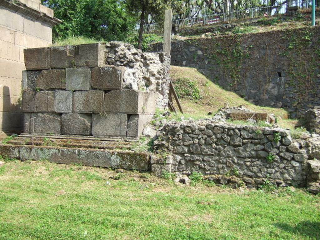 Pompeii Porta Nocera Tombs 19aOS and 19bOS behind 19OS. Looking across 21OS to rear of tomb 19OS.
Tomb 19aOS was an enclosure or recinto at the shoulder of tomb 19OS. It is now completely buried.
A marble columella was found with the inscription 

HELLE  PVEL
LA  VIXIT  AN
NIS  IV.

This reads as 

Helle Puella vixit annis IV

The tomb name is unknown, and according to De Caro, it is unlikely to be that of the four year old slave Helle Puella.
Tomb 19bOS was further to the south behind tomb 19aOS close to the escarpment forming the boundary of the tombs. 
This also is not visible today.
See DAmbrosio, A. and De Caro, S., 1983. Un Impegno per Pompei: Fotopiano e documentazione della Necropoli di Porta Nocera. Milano: Touring Club Italiano. (19aOS, 19bOS).