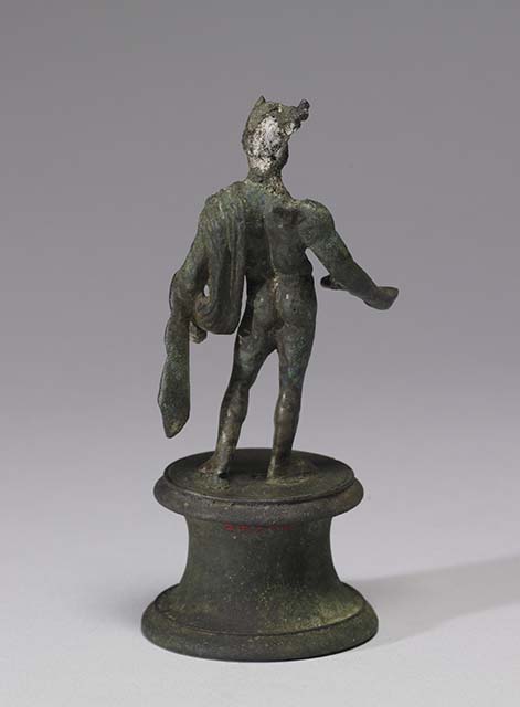 Boscoreale, Villa rustica in fondo DAcunzo. Room 12, lararium. 
According the The Walters Art Museum, this is a bronze statuette of Mercury, front view.
According to Della Corte, this statuette seemed to represent a faun, (0.12 high) naked except for a goat skin between the left shoulder and corresponding elbow.
He has what may be a syrinx? (pan-pipe) held lowered in his right hand. 
Upon his head were two projections on the sides of the forehead, apparently horns, but they were seriously damaged. 
See Notizie degli Scavi di Antichit, 1921, p. 441. According to Stefani, the different. and more plausible interpretation proposed by others is an image of Mercury.
See Stefani G., 2000. In Sylva Mala, Bollettino del Centro Studi Archeologici di Boscoreale, Boscotrecase e Trecase XII, p. 11-16 and note 44.
Photo courtesy of The Walters Art Museum, Baltimore. Inventory number 54.748.
http://thewalters.org/
Creative Commons Attribution-ShareAlike 3.0 Unported Licence
