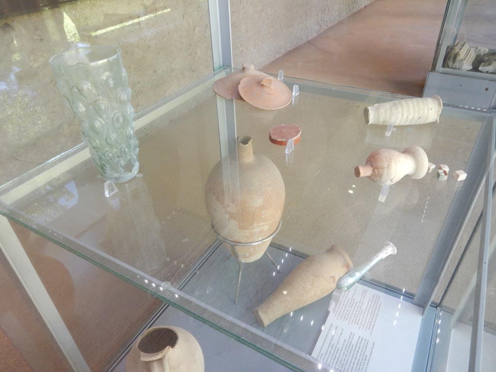 Complesso dei triclini in località Moregine a Pompei. May 2018. Finds on display in Pompeii Palaestra.
Blown glass perfume vessel.
Blown glass drinking cup with drops decoration.
Common ware lids of local production.
Red terra sigillata base from a plate of central-italic origin with the maker mark L(ucius) R(asinius) P(isanus).
Two fritilli used for dice throwing.
Photo courtesy of Buzz Ferebee.

